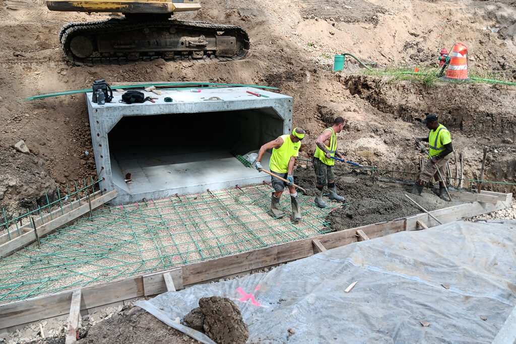 Workers placing and finishing concrete around a box culvert outlet structure