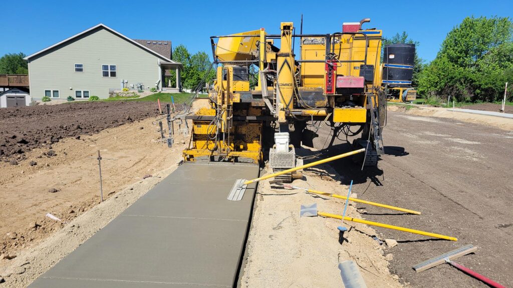 Concrete paving machine laying fresh sidewalk along a residential street under construction