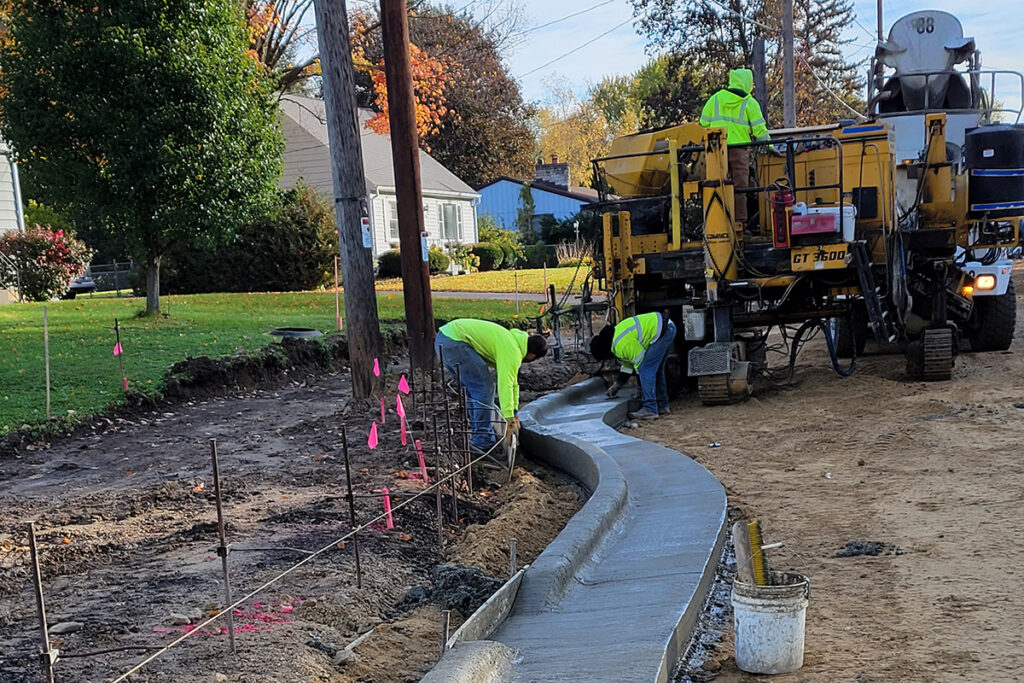 Workers pouring and shaping a curved concrete curb with a paving machine