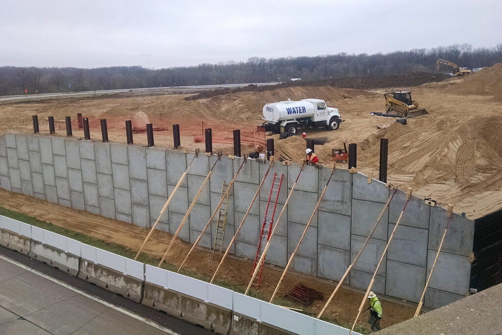 Workers constructing a retaining wall with concrete panels at a large earthwork site