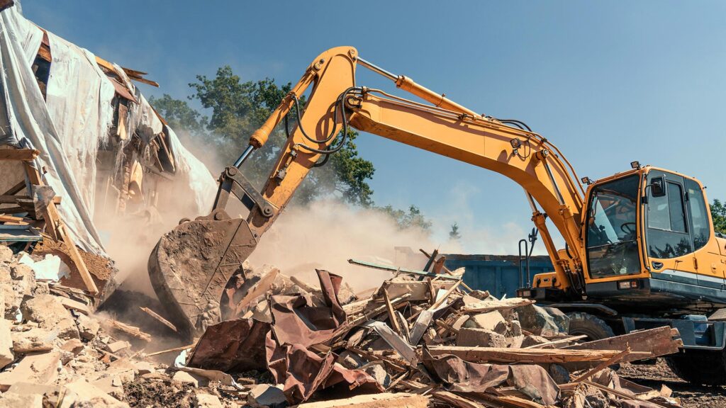 Excavator demolishing a building and clearing debris at a construction site