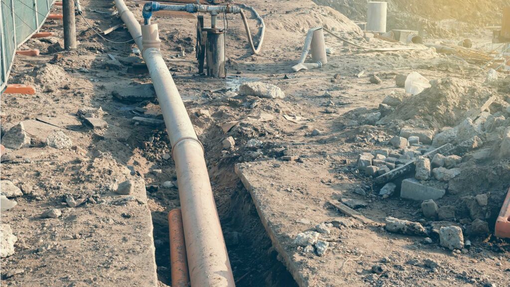 Large pipe installed in an open trench at a construction site with dirt and debris surrounding it