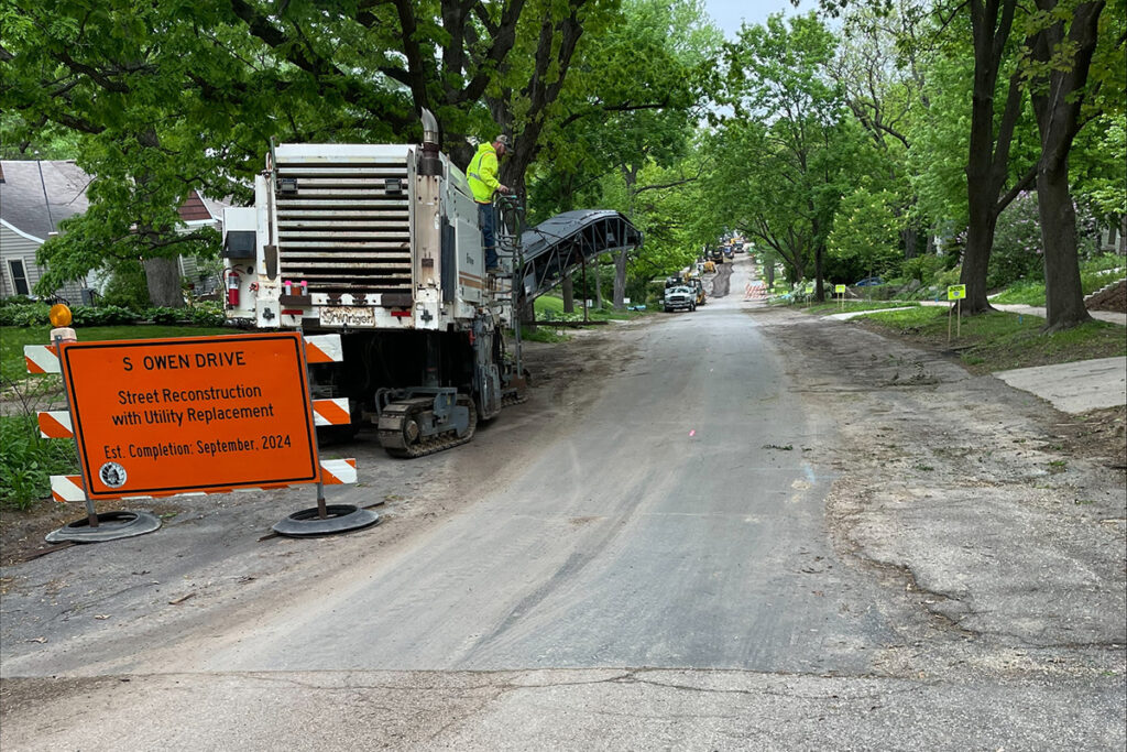 Road construction site with milling machine and signage for utility replacement project