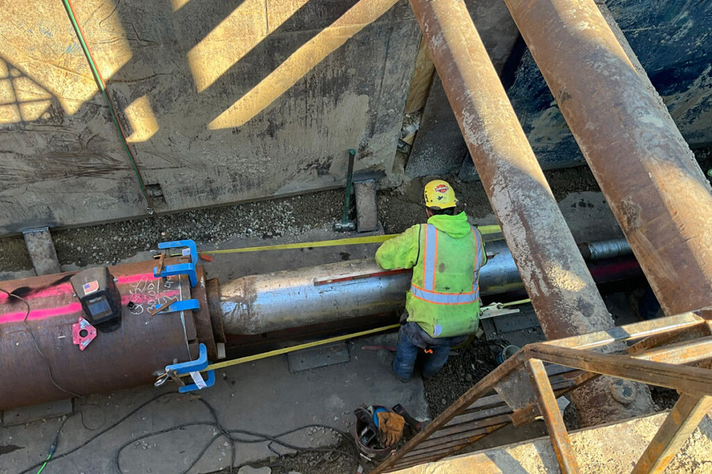 Worker measuring and aligning a large pipe inside a shored trench