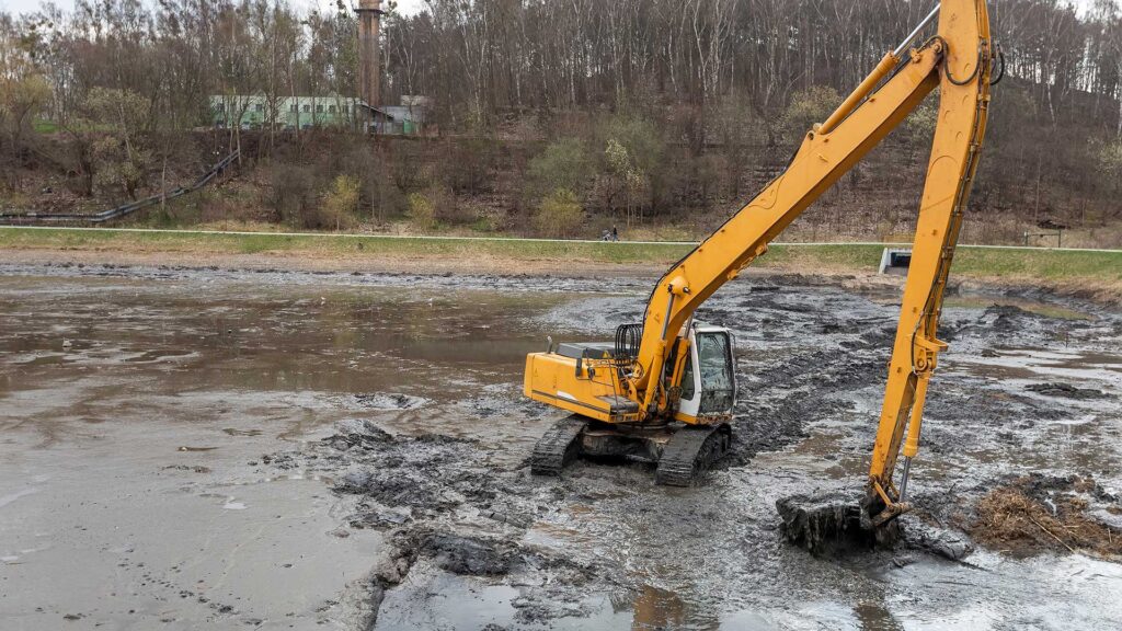 Excavator digging through mud in a drained pond during cleanup work