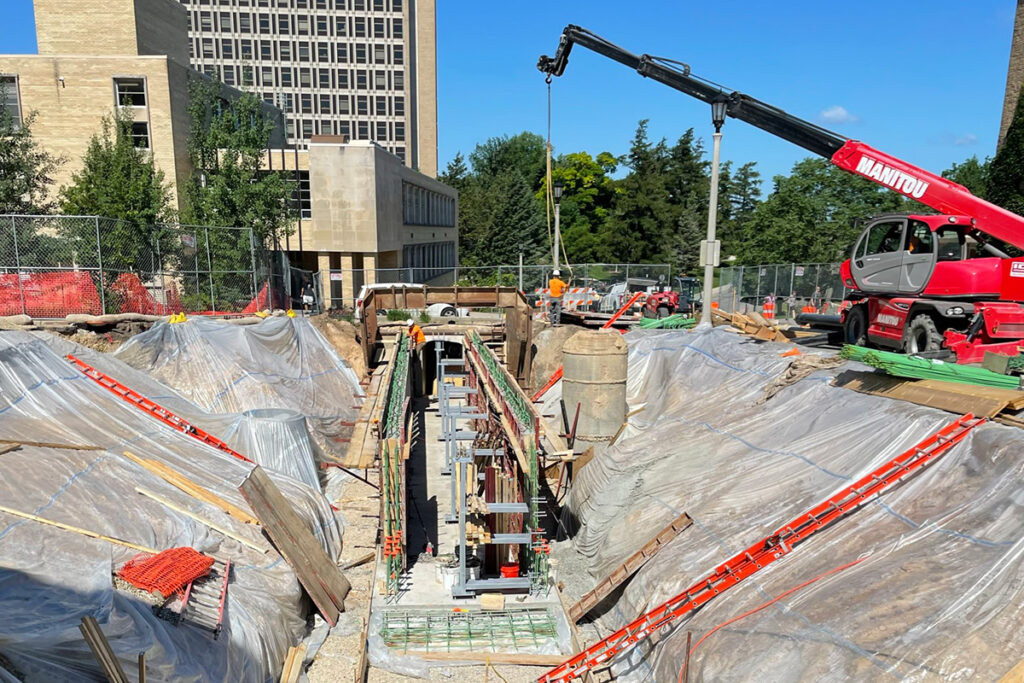 Construction crew working in a trench with a crane lifting materials at an urban job site