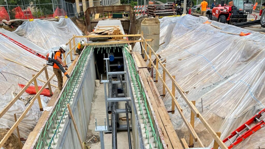 Construction workers installing underground utility pipes in a trench with protective coverings