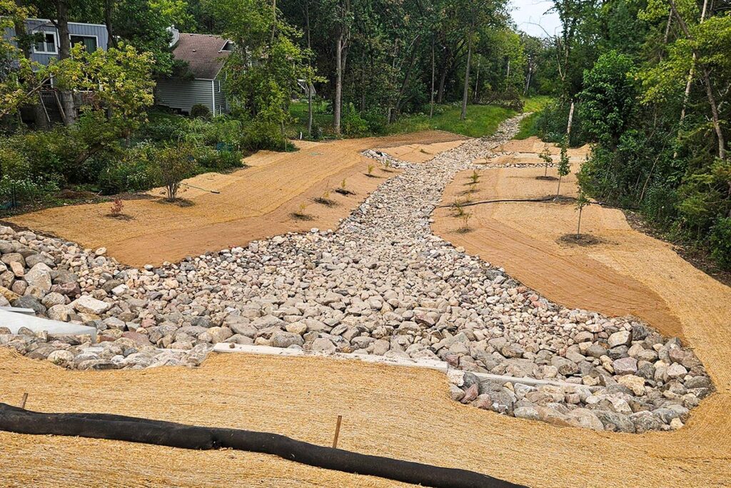 Landscaped drainage channel with rocks and erosion control in a wooded residential area