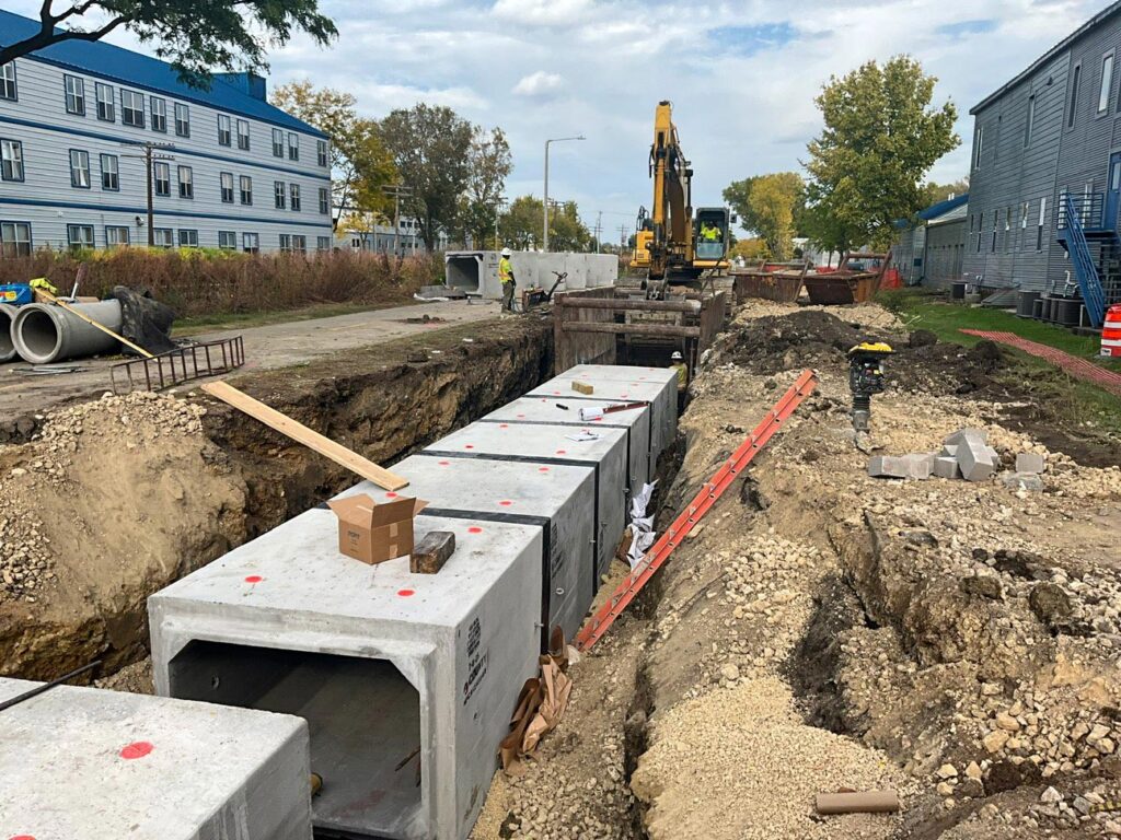 Precast concrete box culverts being installed in a trench with an excavator and crew